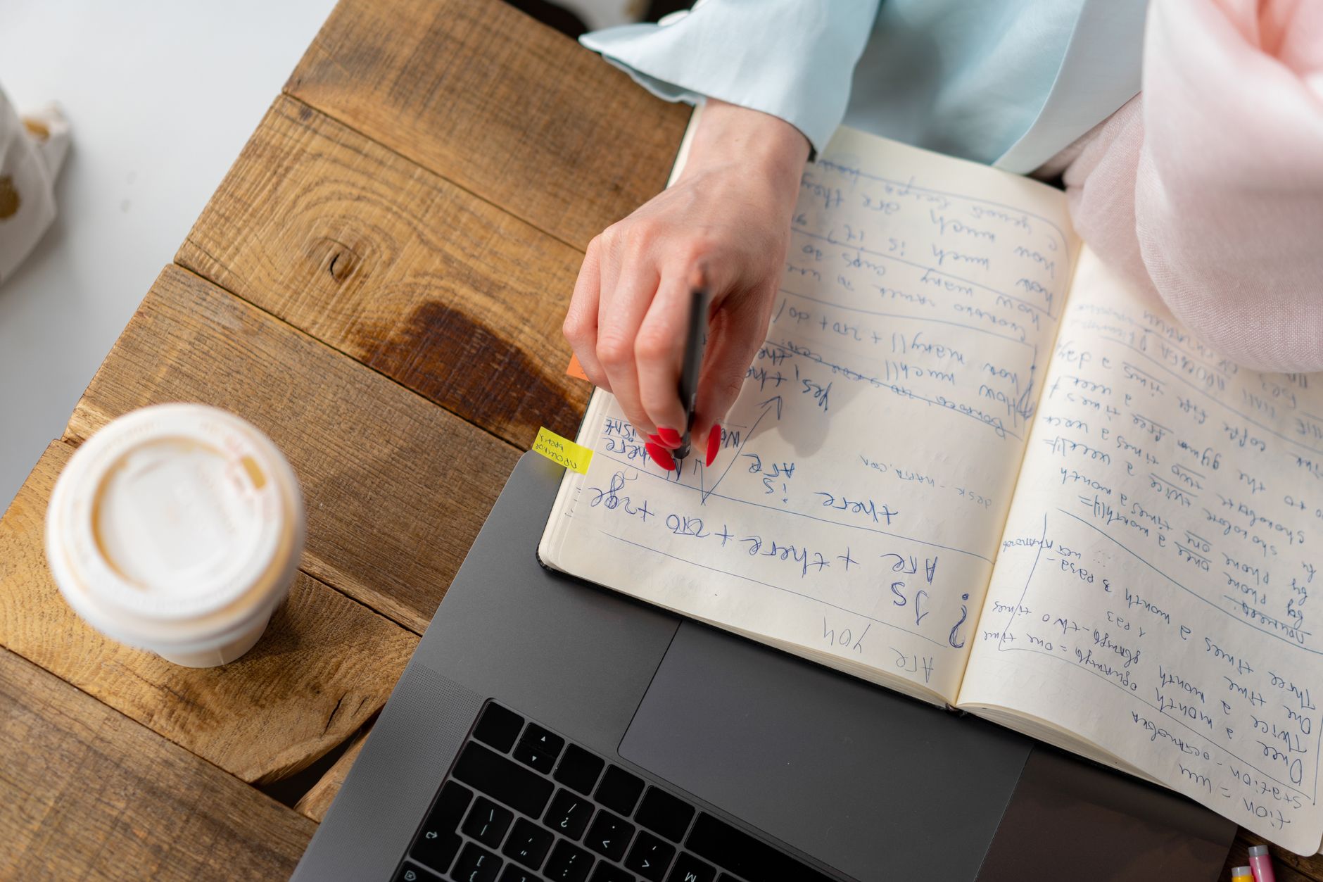 A tidy desk with a laptop, coffee cup, pen, and notebook showing a minimal workspace.